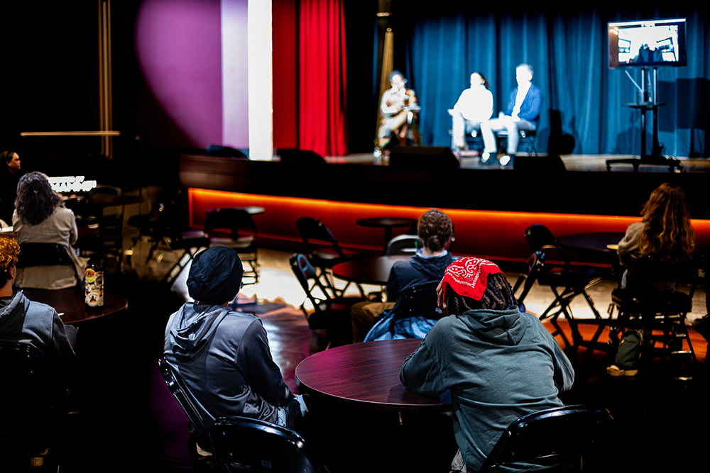 An audience watching three speakers onstage.