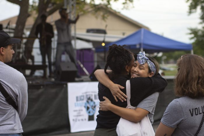 Two women hugging in front of a political booth at an event, showcasing community building.
